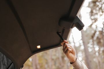 Unrecognisable man holds trunk handle and closes car trunk door outdoors in park. Interior details...