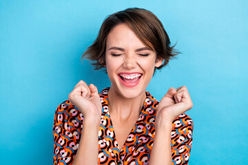 Photo of delighted satisfied girl closed eyes raise fists scream yes hooray isolated on blue color background