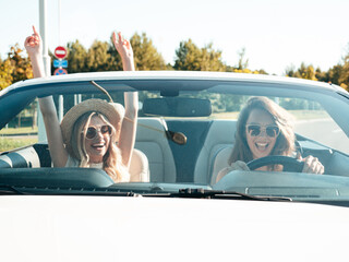 Portrait of two young beautiful and smiling hipster female in convertible car. Sexy carefree women...