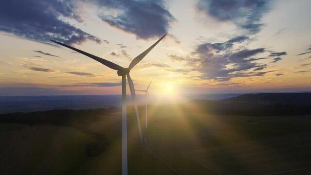 A footage of a two wind power turbines in a row in operation against dramatic sky with setting sun.