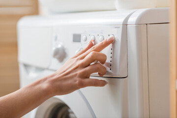 Cropped view of woman tuning white washing machine in laundry room.
