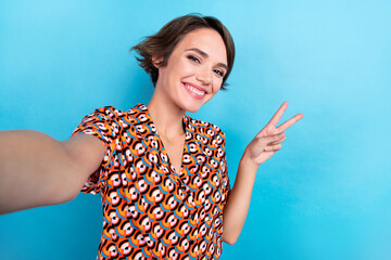 Photo of lovely cheerful person make selfie toothy smile demonstrate v-sign isolated on blue color background