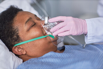 Close up of nurse placing oxygen support mask on senior patient in hospital room