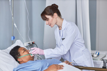 Side view portrait of caring nurse placing oxygen support mask on senior patient in hospital room