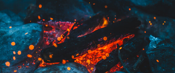 Vivid smoldered firewoods burned in fire closeup. Atmospheric background with orange flame of campfire. Wonderful full frame image of bonfire with glowing embers in air. Warm logs, bright sparks bokeh