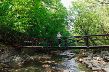 a woman stands on a bridge over a river in a green forest