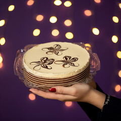 New Year's holiday cake in hands of woman. Christmas baking. Layered cake on purple background with...