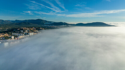 Naklejka na ściany i meble Aerial view, flight above the clouds, the coast of Mallorca in the fog with the town of Santa Ponca, Mallorca, Spain