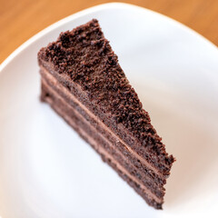 Piece of chocolate cake Prague on white plate. Festive dessert with chocolate cream. Cake layers. View from above. Close-up. Soft focus. Copy space.