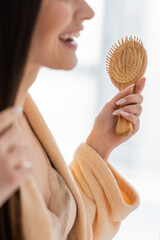 cropped view of happy young woman holding wooden hair brush in bathroom.