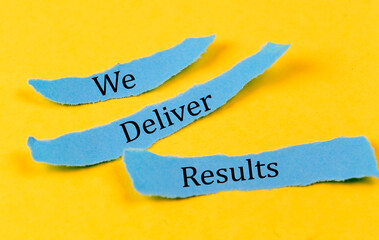 WE DELIVER RESULTS text on a blue pieces of paper on yellow background, business concept
