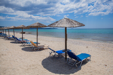 A tranquil beach scene with an idyllic horizon over the blue sea, a straw parasol for shade and a lounge chair to relax in , perfect for summer holidays.