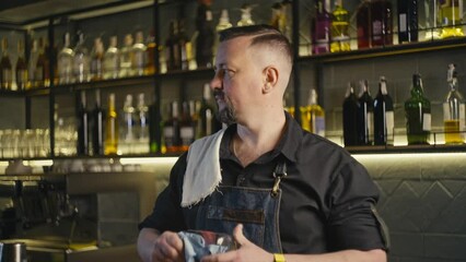 Slow motion video of a Caucasian bartender wiping a beer glass with a towel. Professional work and service at the bar. - Powered by Adobe