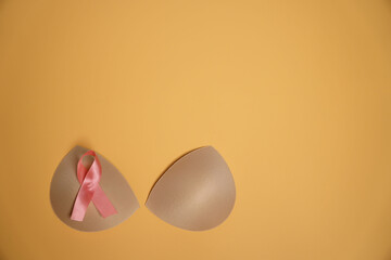 Breast cancer awareness concept.Top view photo of pink ribbon bra support pad on isolated orange background with copy space,Concept of breast augmentation surgery