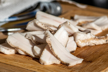 Fototapeta premium Pieces of lard or bacon, sliced thinly for consumption, on a wooden cutting board in a street food market, close up