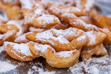 Fried pastrie of Carnival, strips of fried dough typically made on Mardi Gras covered by powdered sugar, close up - obrazy, fototapety, plakaty