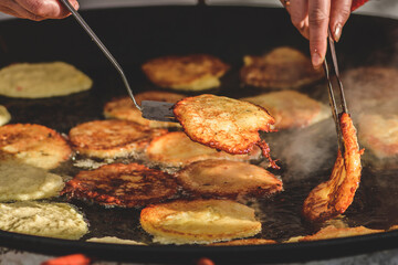 Frying traditional blini, blin or bulviniai blynai, potato pancakes on an open fire in a street food market