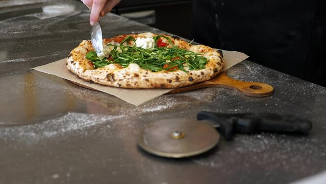 Close-up of a chef putting stracciatella cheese on a ready freshly baked pizza in an Italian pizzeria.
