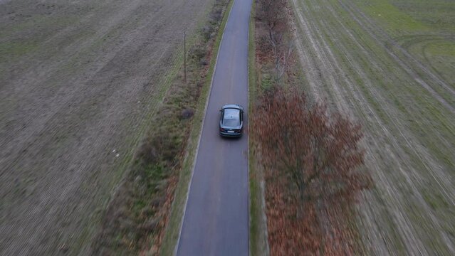 The car is driving on the road in the field. Flying over the car. Video from a drone. Green meadow. The car makes a figure of eight. The car goes like in the movies. Summer landscape