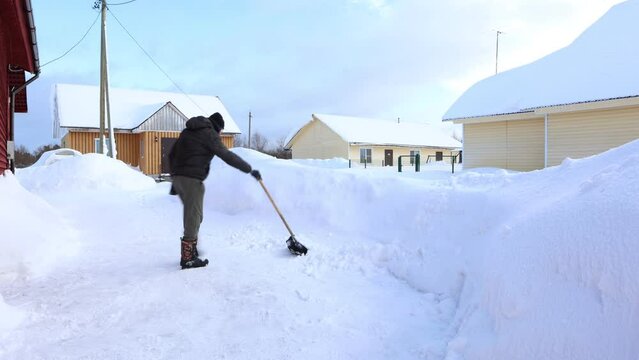 Man uses snow shovel to clear snow drifts in his yard.
