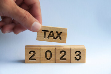 Hand holding wooden block with text TAX 2023. Taxation concept