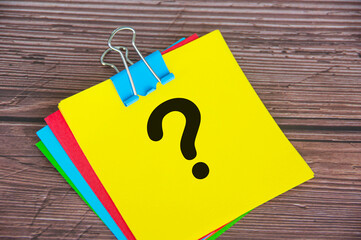 Question mark on yellow notepad with wooden desk background. Motivational concept.