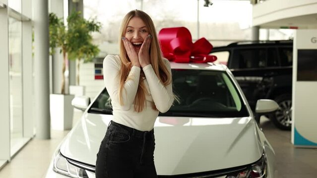 Woman surprised by her new car standing in car showroom with a huge red bow on top