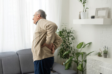 Caucasian old senior elderly unhealthy sickness grey male grandpa near sofa at home alone holding...