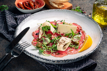 Beef carpaccio with parmesan, arugula and capers on a white plate. Italian dish starter, dark...