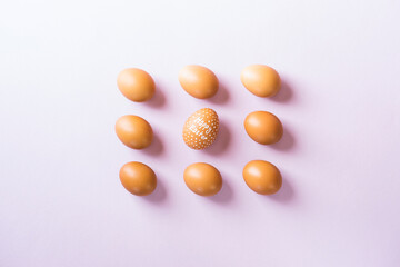 Nine brown eggs flat lay on purple background with one Happy Easter witten egg