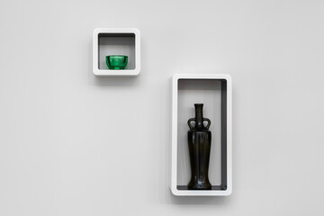 Interior decor items a bottle and a cup stand inside square shelves against a white wall