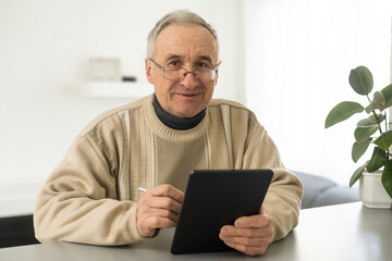 Smiling senior man reading news on digital tablet. Cheerful excited mature male using portable computer at home, copy space.