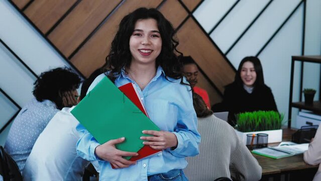 Portrait of Happy smiling middle eastern turkish female student standing in class, holding books and looking at camera. Classmates students are on background. Study at college, education concept. 