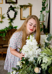 portrait of  blonde beautiful  girl with long hair and in light dress with a bouquet of flowers in light room  with flowers on sunny day