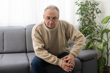 old man with his knee joint pain in sofa, pain in the elderly, health care, elderly care. Elderly man having a knee pain and sitting down. Grandfather with knee pain.