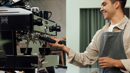 Cropped shot of a young barista using a coffee machine. Smiling male barista adjusting coffee machine.