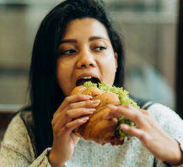 A young African American woman sits in a cafe and eats an appetizing burger. Bad cheap food. Wrong...