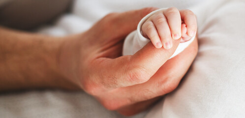 Close up photo of father holding newborn baby hand.