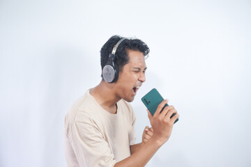Fototapeta premium Energized man sings to music, moves actively, wears headphones and casual t shirt, poses against white background, keeps mouth widely opened, enjoys life, isolated on white studio wall