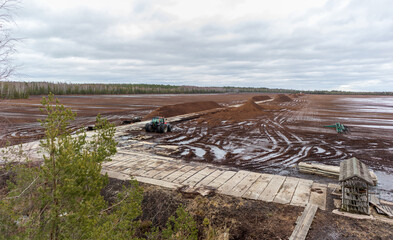 Fototapeta na wymiar Nature view of a swamp with a peat digging site in a swampy area with a wooden boardwalk and a tractor in the background