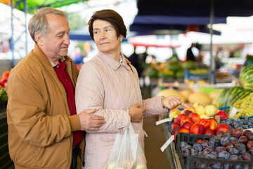 Aged man and woman customers buying peaches in open-air market