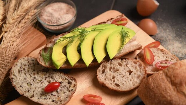 sliced avocado with dill leaves on baguette bread on black background, home made bakery concept.pan motion