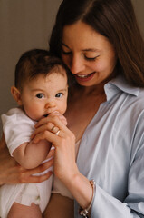 The portrait of young brunette mom in blue skirt looking to her naked sweet baby girl who is smiling directly at the camera; mother's day background 