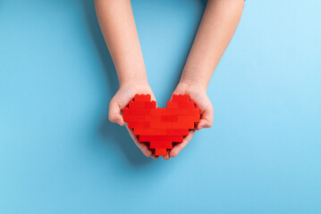 Fototapeta premium Hands of little girl child holding heart made of plastic bricks on blue background