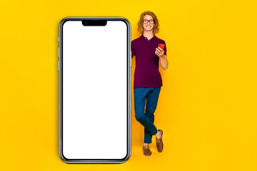Full length photo of funky ginger guy stand hold telephone wear eyewear t-shirt jeans pants sneakers isolated on yellow background