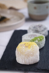 A traditional Japanese fresh homemade rice mochi bun with green orange yuzu citrus filling top with zuyu power, plate and cup of tea in background 