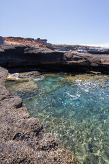 Views of a volcanic rocky cliff. Turquoise ocean. Gray volcanic rock formation. La Caleta, Tenerife, Canary Islands Spain.