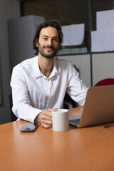 portrait d'un jeune homme souriant, employé de bureau assis devant son ordinateur au bureau.