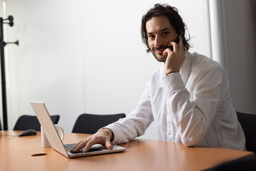 portrait d'un jeune homme souriant, employé de bureau assis devant son ordinateur au bureau. Il...