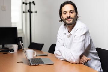 portrait d'un jeune homme souriant, employé de bureau assis devant son ordinateur au bureau.